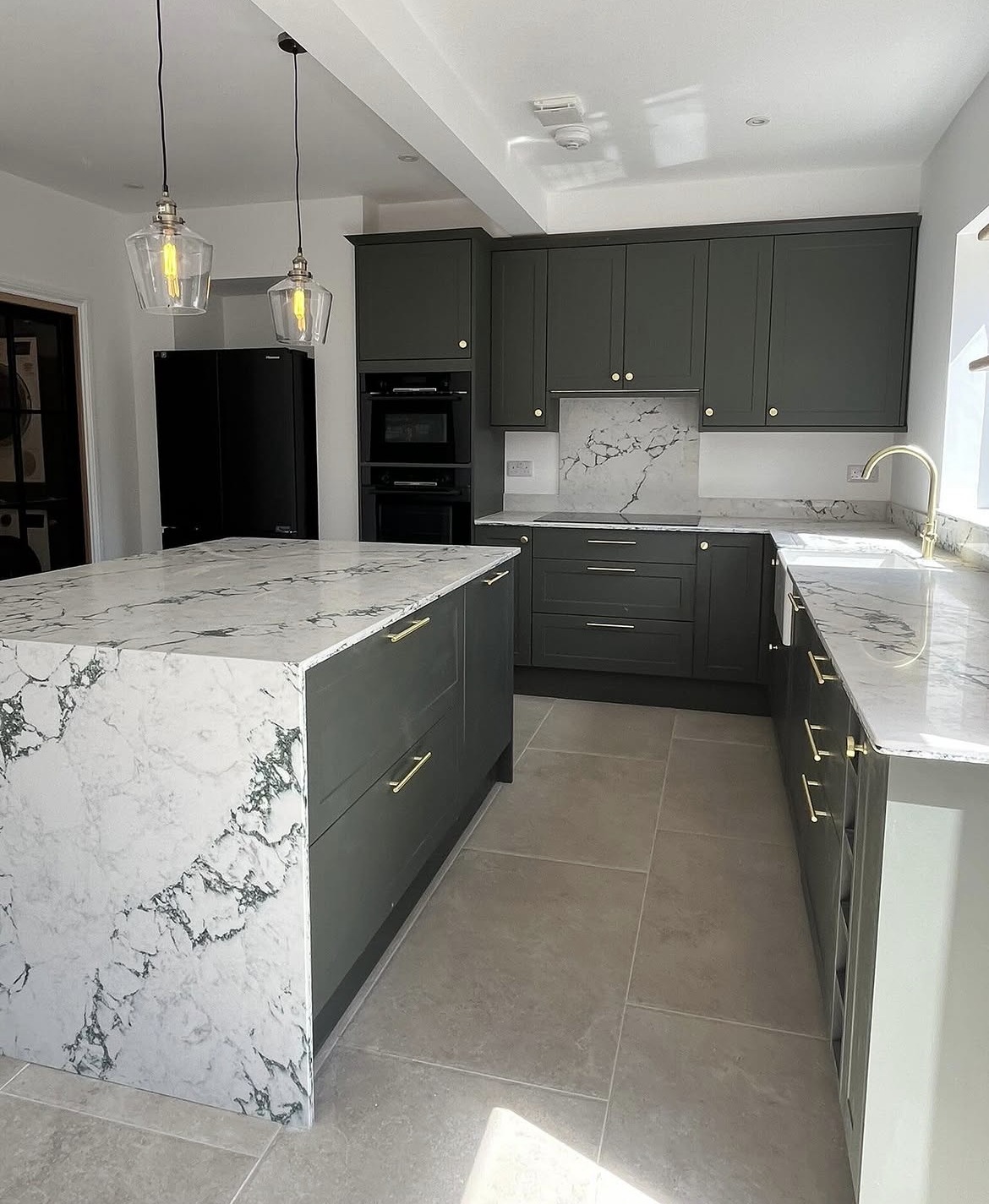 Refurbished kitchen with dark green cabinetry, marble-effect island and brass handles