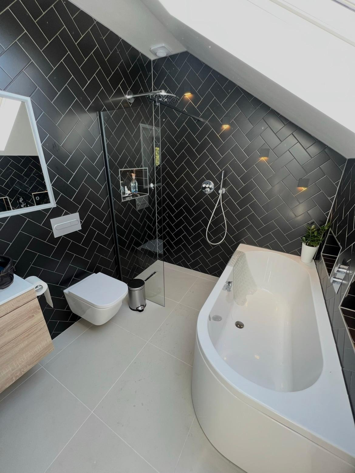 Fully refurbished loft bathroom with black herringbone tiling, walk-in shower and freestanding bath
