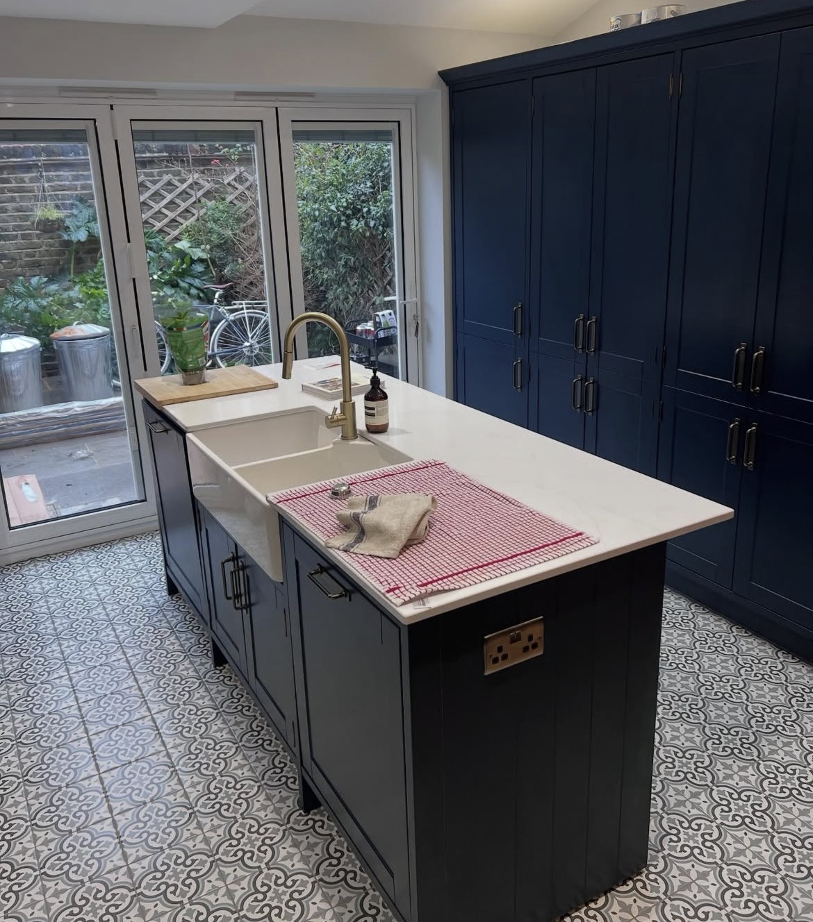 Kitchen island with white worktops and patterned tiled floor in a renovated home