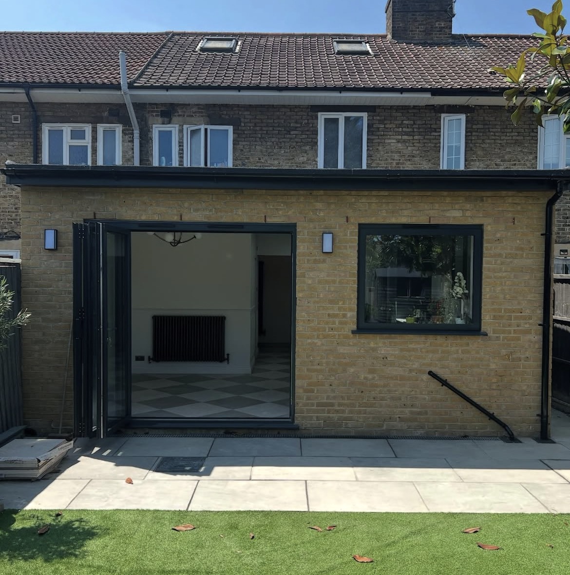 Rear elevation of a completed yellow brick single-storey extension with black-framed glazing