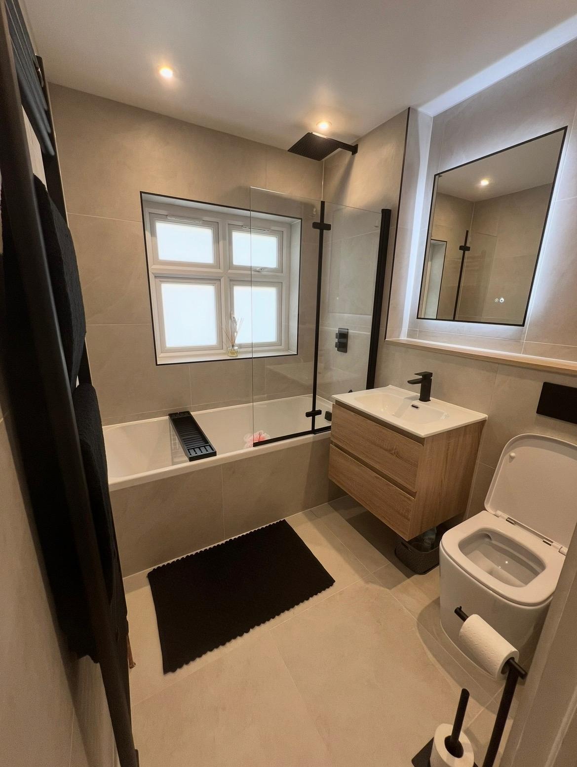 Newly tiled bathroom with bath-shower combination and black fittings after a full bathroom refurbishment