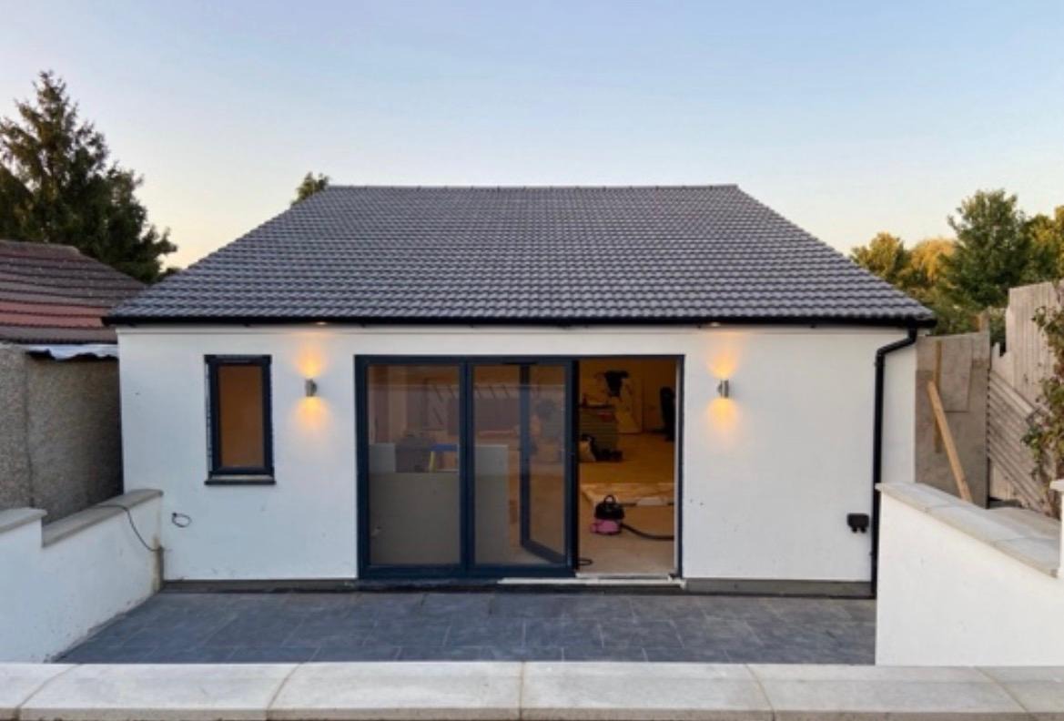 Completed rendered garden outbuilding with dark-framed glazing and exterior lighting