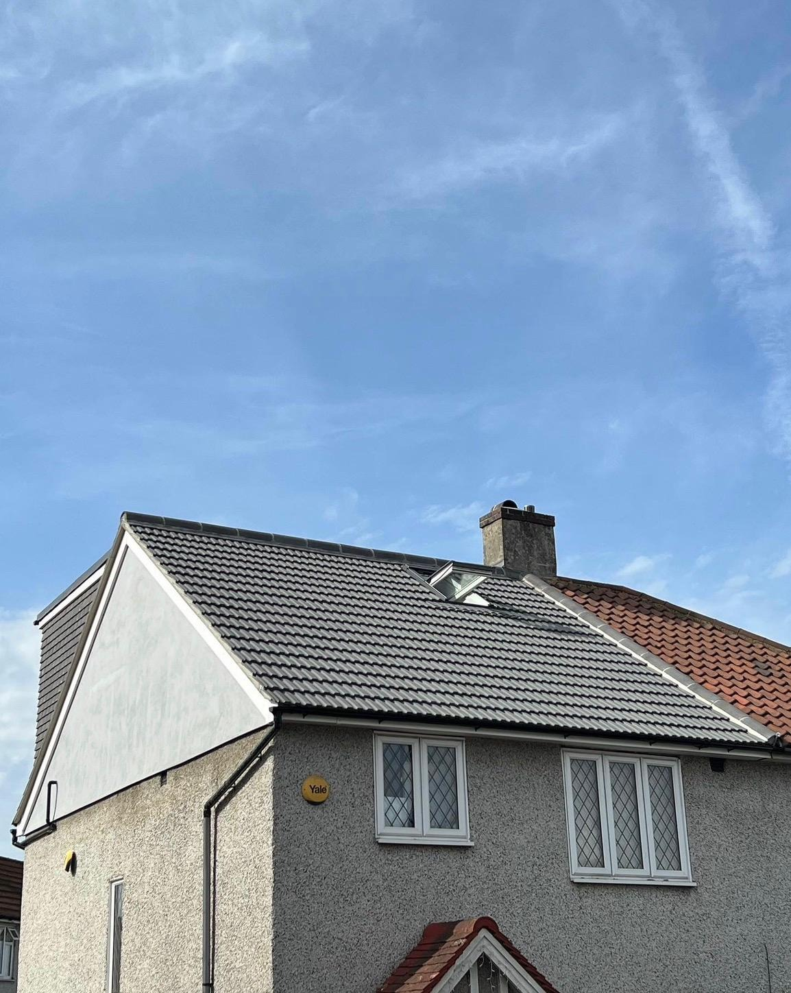 Newly re-tiled pitched roof with dark grey tiles, rooflight and leadwork on a rendered semi-detached house