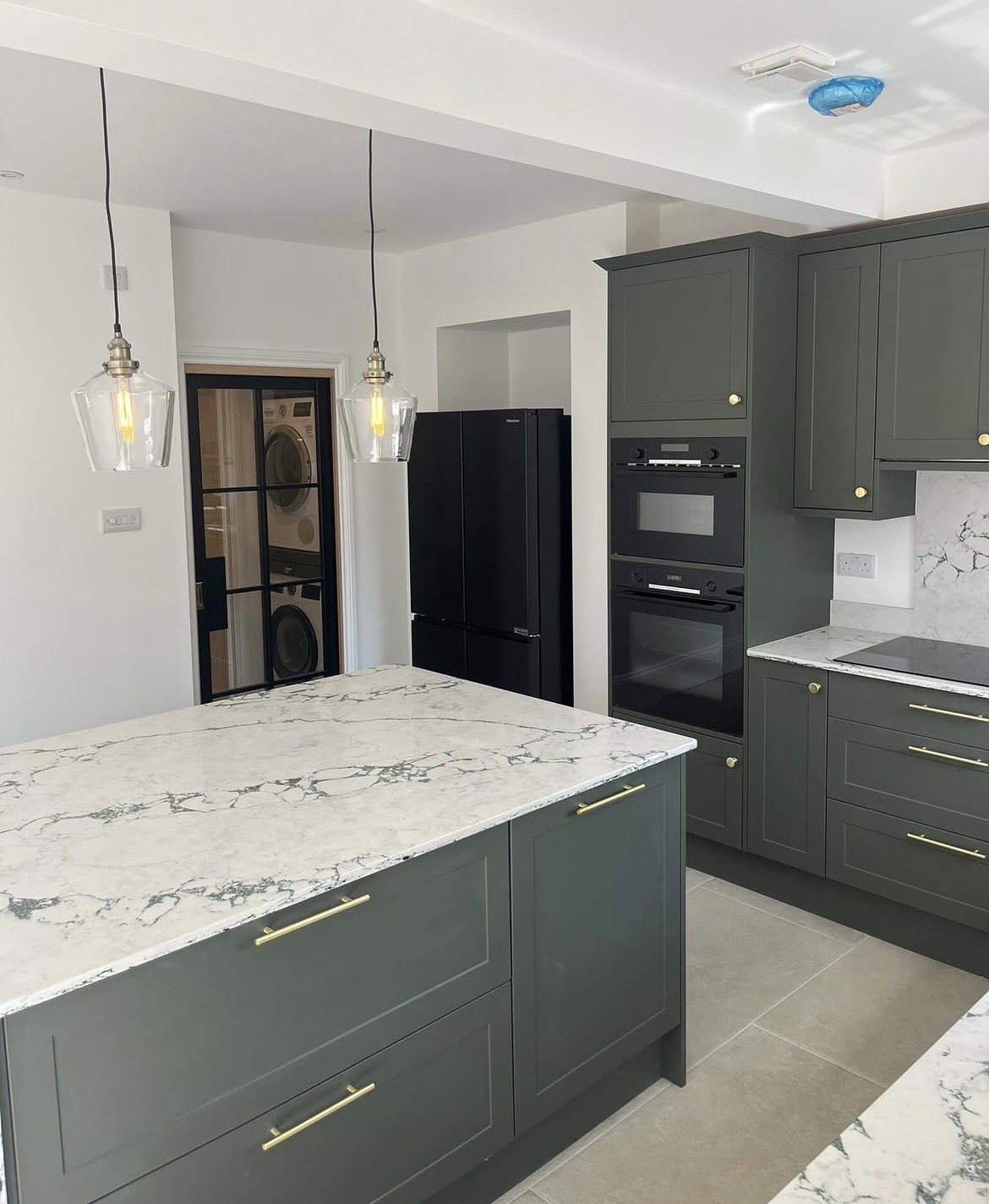 Green shaker kitchen with marble-effect worktops and integrated appliances after refurbishment