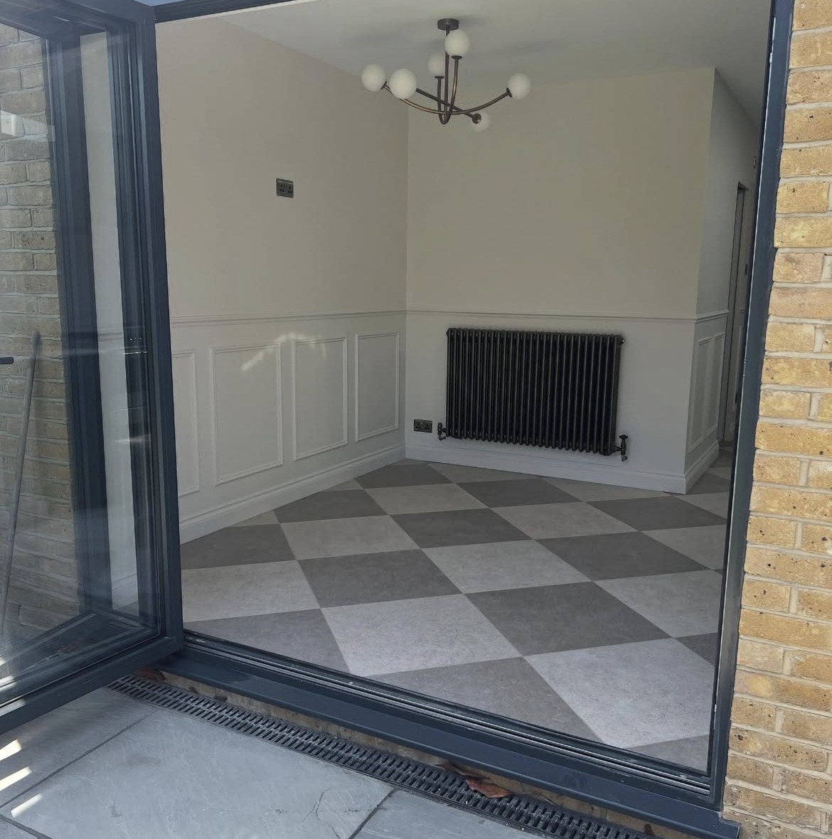View through the glazed doors of a completed rear extension with panelled walls and chequerboard flooring